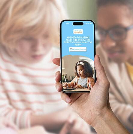 Hand mit Smartphone, das KUMON Connect App zeigt, vor Lernsituation mit Kindern und Lehrerin.