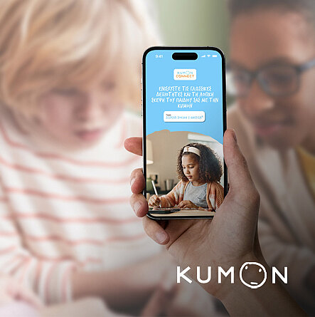 Hand mit Smartphone, das KUMON Connect App zeigt, vor Lernsituation mit Kindern und Lehrerin.