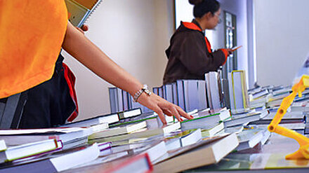 Bildungskommunikation? Frauenhand greift ein Buch in einer Bücherauslage.