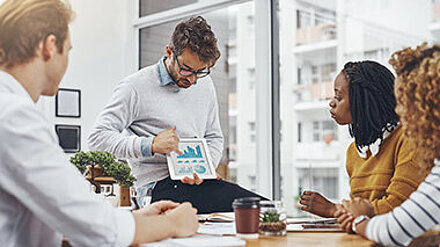 Challenge accepted Eine Gruppe Personen bekommt Daten in einem Meetingraum präsentiert.