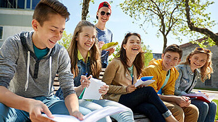 Eine Gruppe Schüler und Schülerinnen sitzt lachend mit Lernmaterialien im Freien.