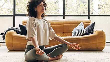 Beautiful Morning Routine Junge Frau sitzt im Schneidersitz im Wohnzimmer und meditiert.