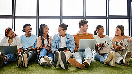 Hiring Gen Z? Gruppe junger Menschen sitzt lachend mit Notizbüchern, Tablet und Laptop zusammen.