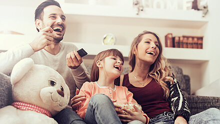 Is Linear TV Rising Again? Parents and their daughter are sitting on the couch, watching TV and laughing.