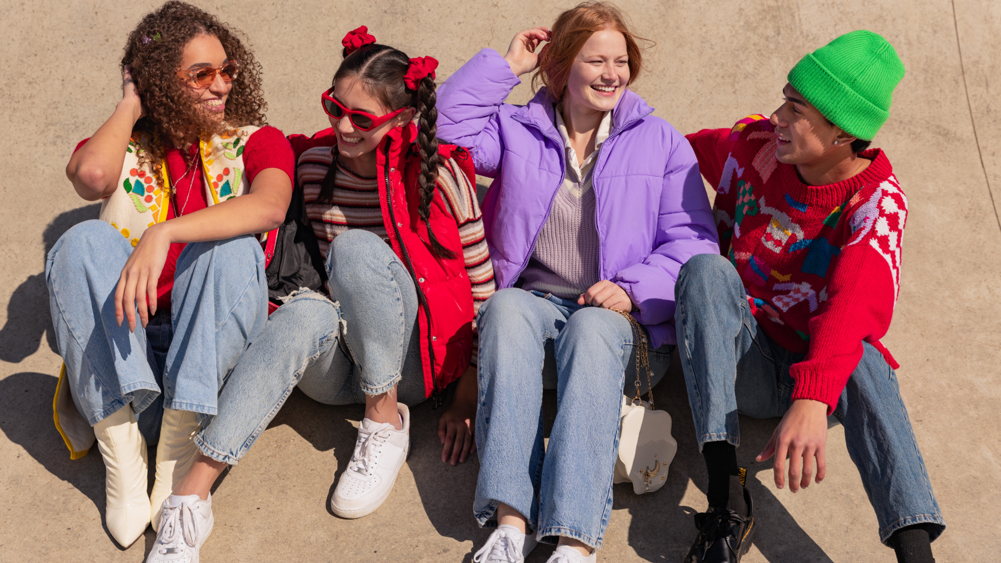 Un grupo de amigos sentados juntos al aire libre, vestidos con ropa colorida y moderna, compartiendo risas y disfrutando de un momento relajado y alegre.