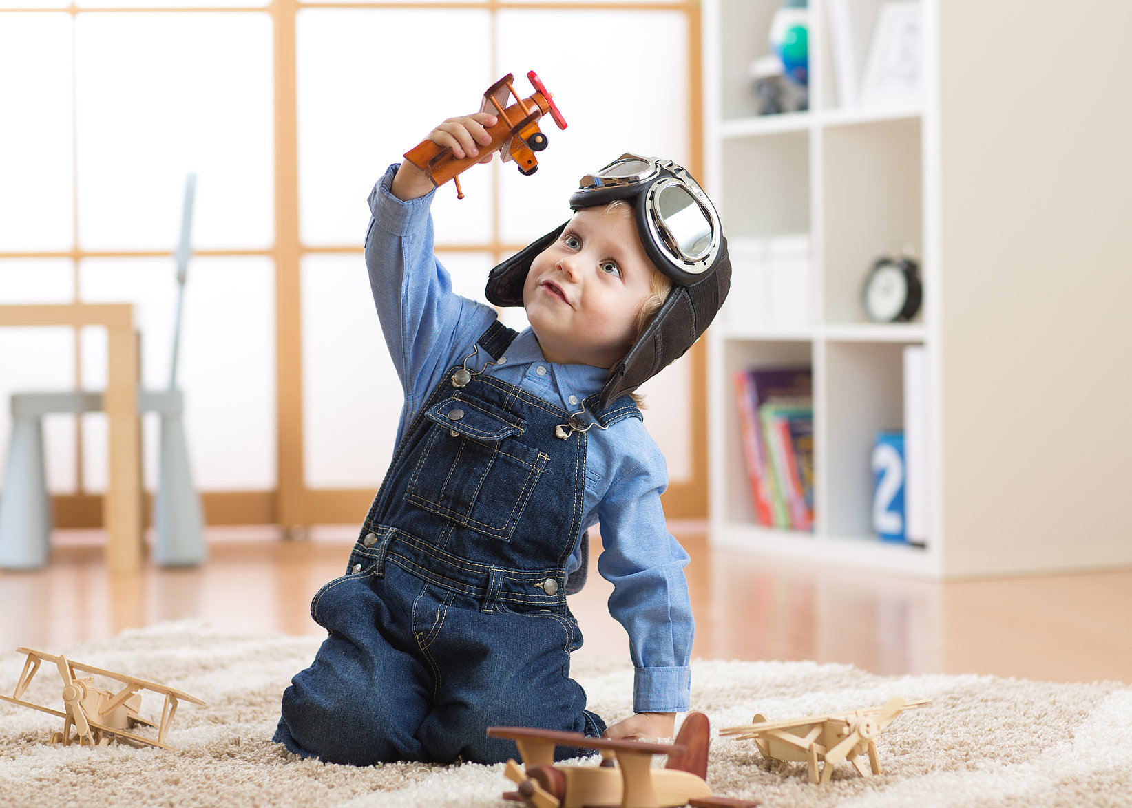 A little boy plays enthusiastically with an aeroplane toy and wears a pilot's cap.