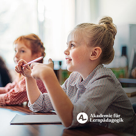 Kinder sitzen an einem Tisch mit Stiften in der Hand und hören aufmerksam zu