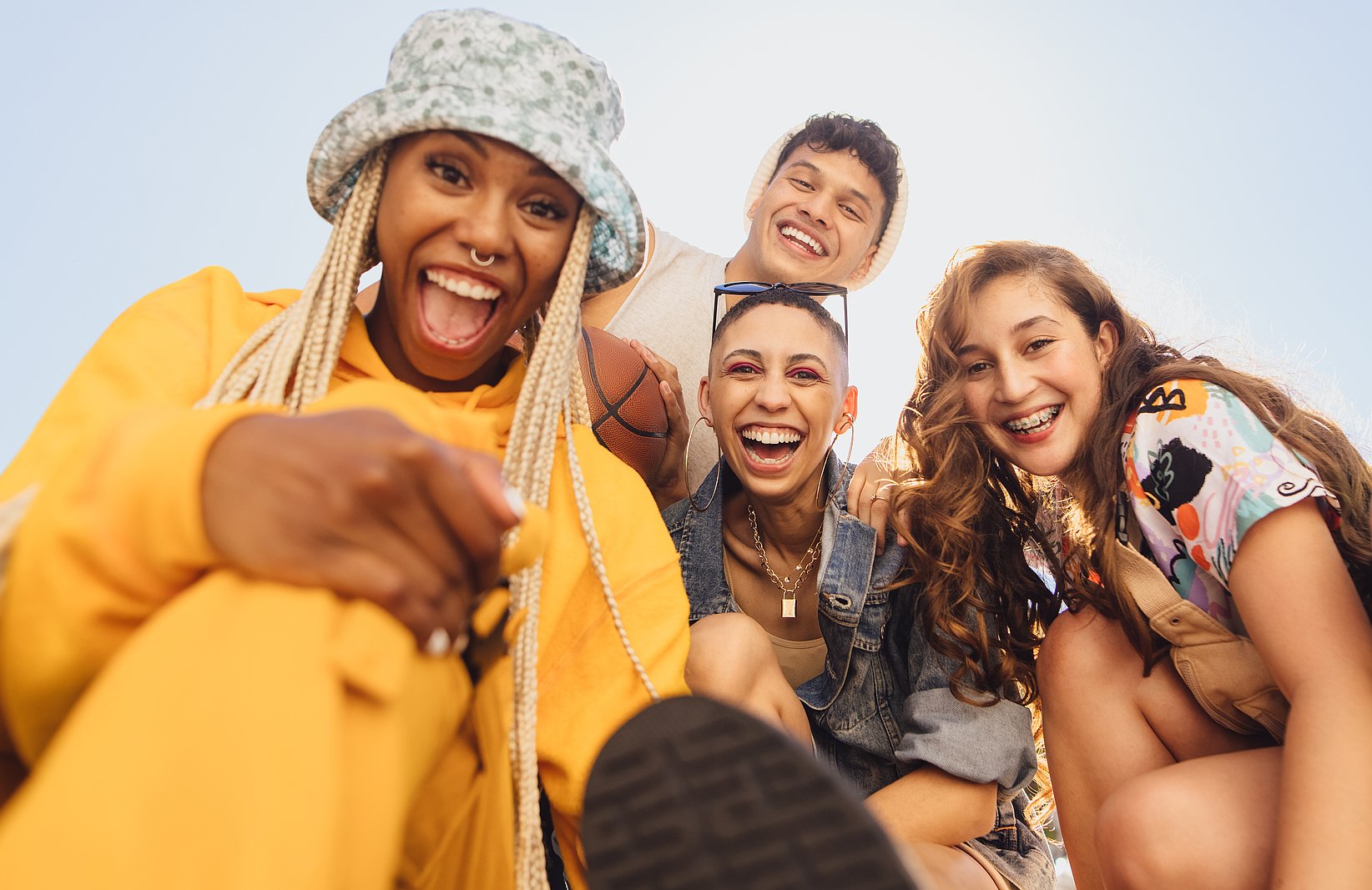 Three women and a man of young age and from different backgrounds look into the camera and all have a smile on their faces.