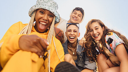 Gen Z's Mental Health - What is Impacting It and What are They Doing About It? Three women and a man of young age and from different backgrounds look into the camera and all have a smile on their faces.