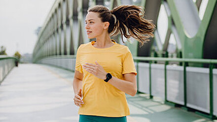 Next Gen Trends & Neujahrsvorsätze 2026 Junge Frau in gelbem T-Shirt joggt über eine Brücke.