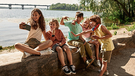 Designing Experiences For Generation Alpha Two girls and three boys are sitting on a wall and making different faces while a girl takes the picture.