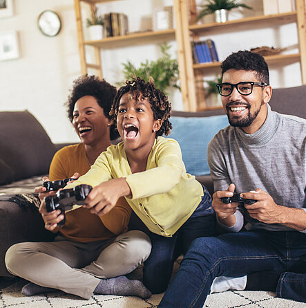 Eltern spielen mit ihrem Sohn ein Videospiel und lachen