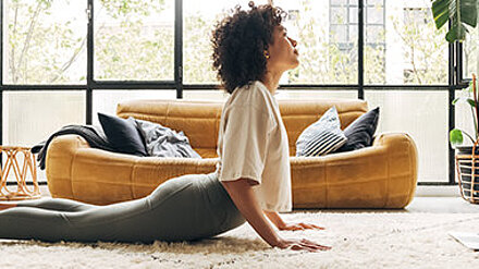 Fitnesshype trifft Lernalltag Junge Frau macht Yoga im Wohnzimmer auf einer Yogamatte.