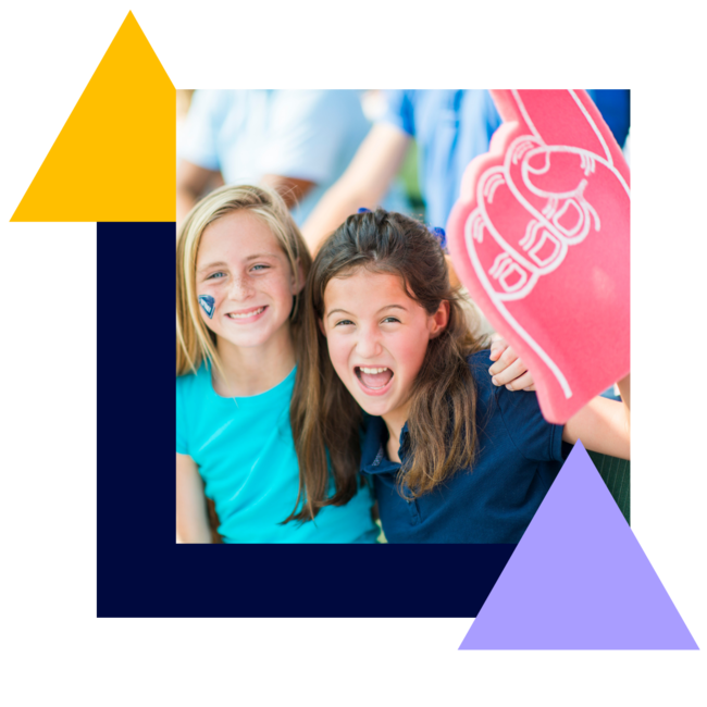 Two little girls look happily into the camera while laying their arms over each other. One girl is holding a large hand balloon with the index finger stretched upwards.