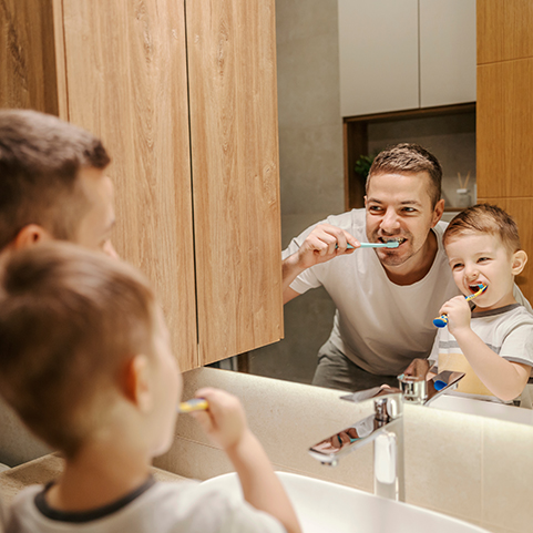 Vater und Sohn putzen gemeinsam vor dem Badezimmerspiegel ihre Zähne.