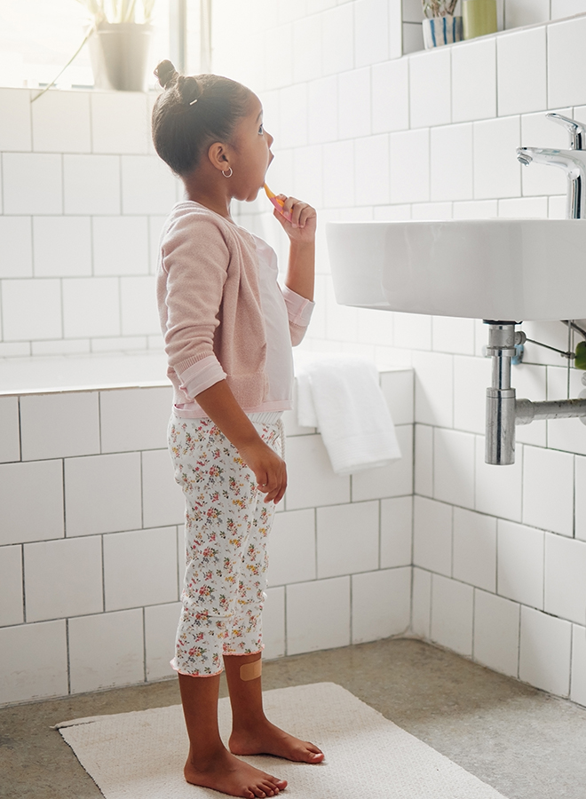 Mädchen steht im Bad und putzt ihre Zähne.