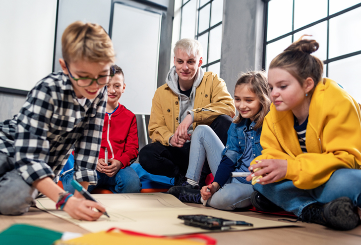 Mehrere Kinder arbeiten gemeinsam mit einer jugendlichen Person an einer Präsentation.