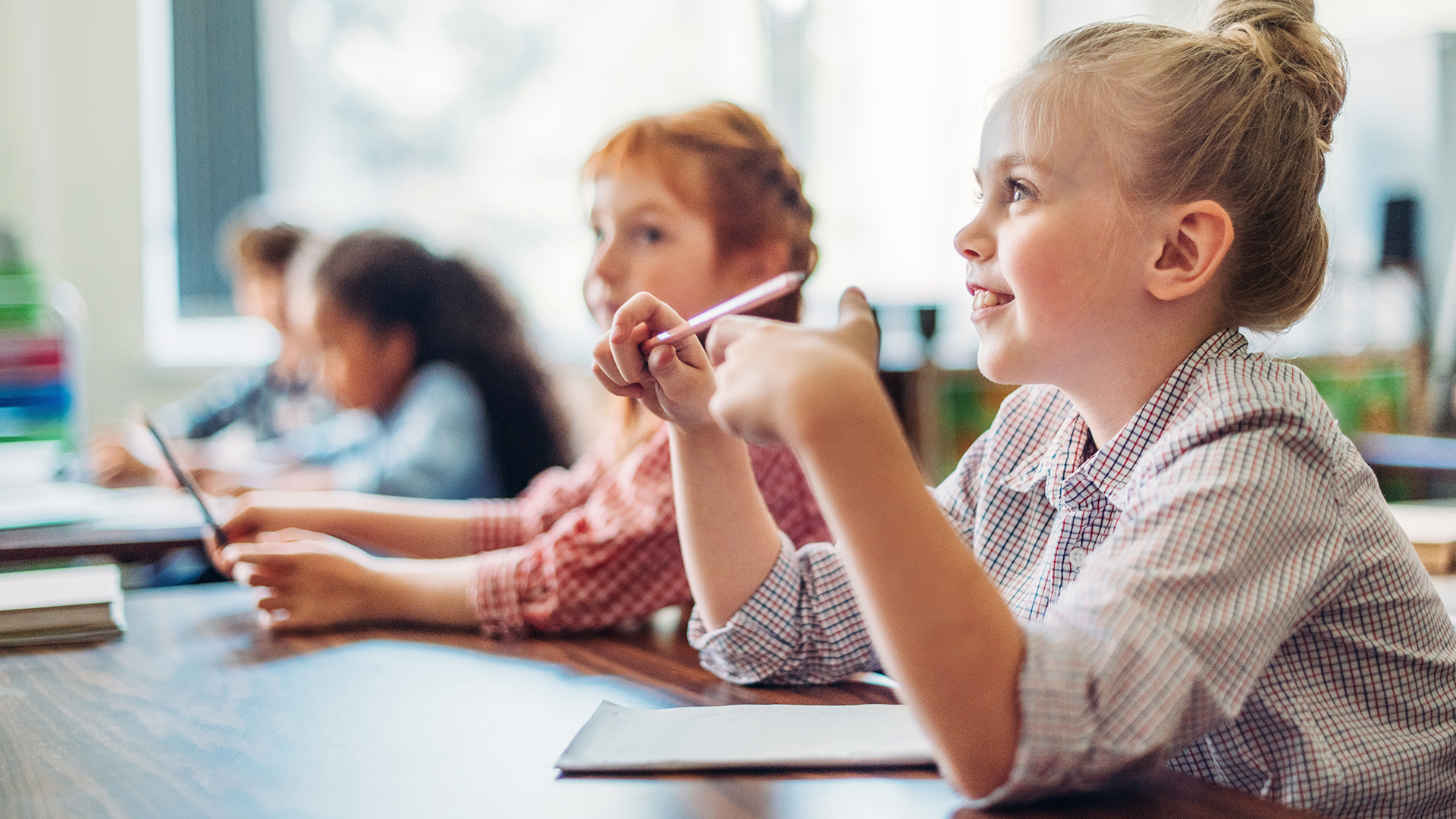 Kinder sitzen an einem Tisch mit Stiften in der Hand und hören aufmerksam zu