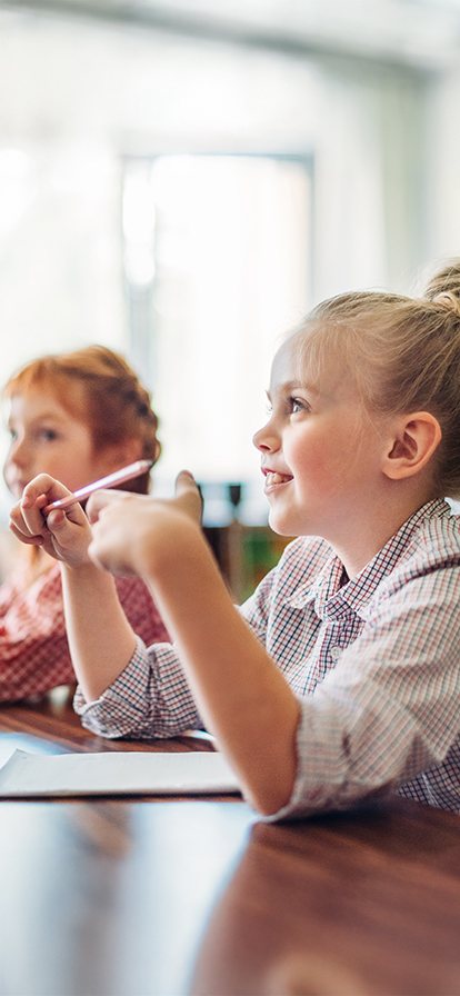 Kinder sitzen an einem Tisch mit Stiften in der Hand und hören aufmerksam zu