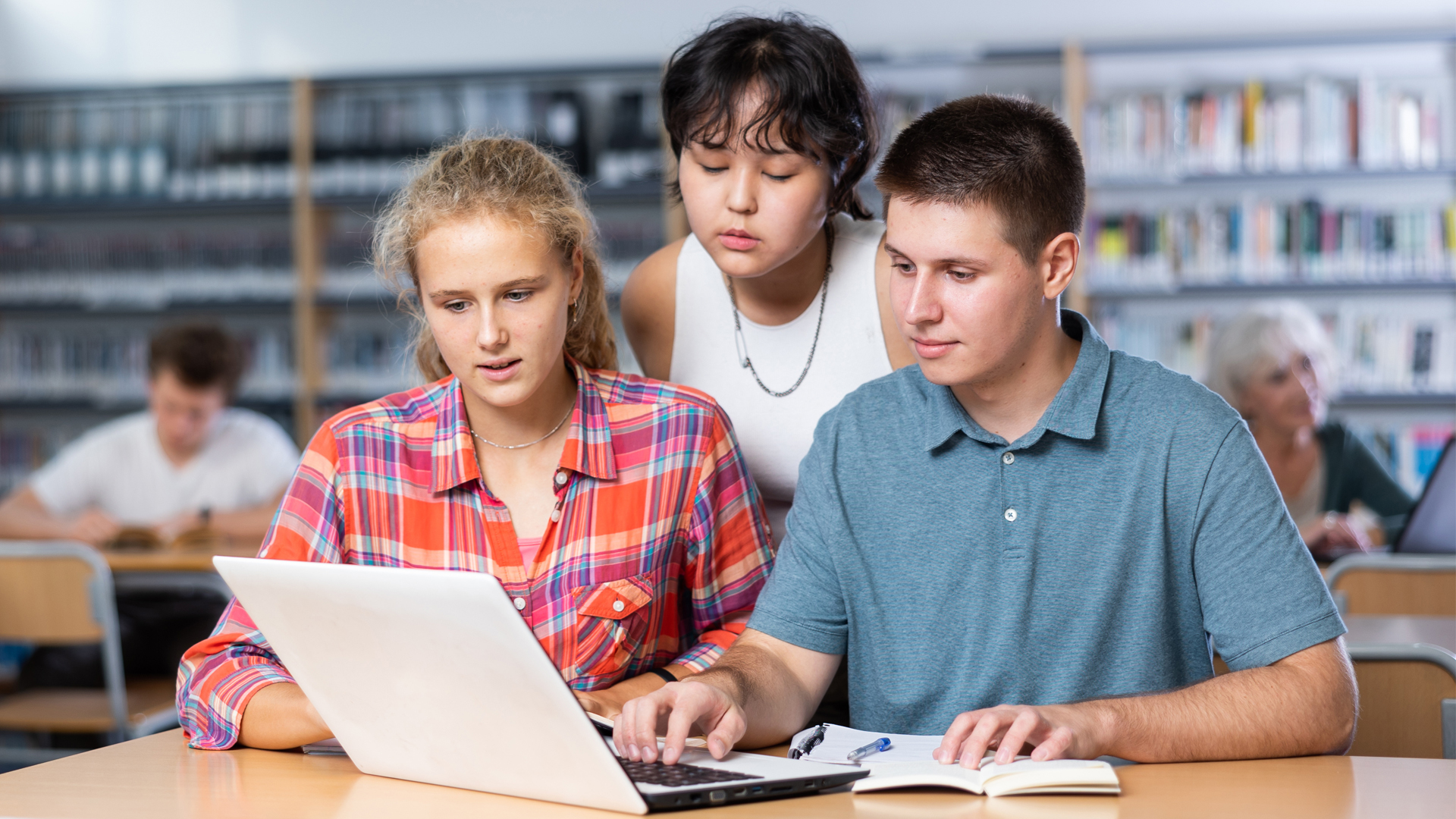 Gruppe von Schülerinnen und Schülern mit einem Laptop in der Bibliothek.