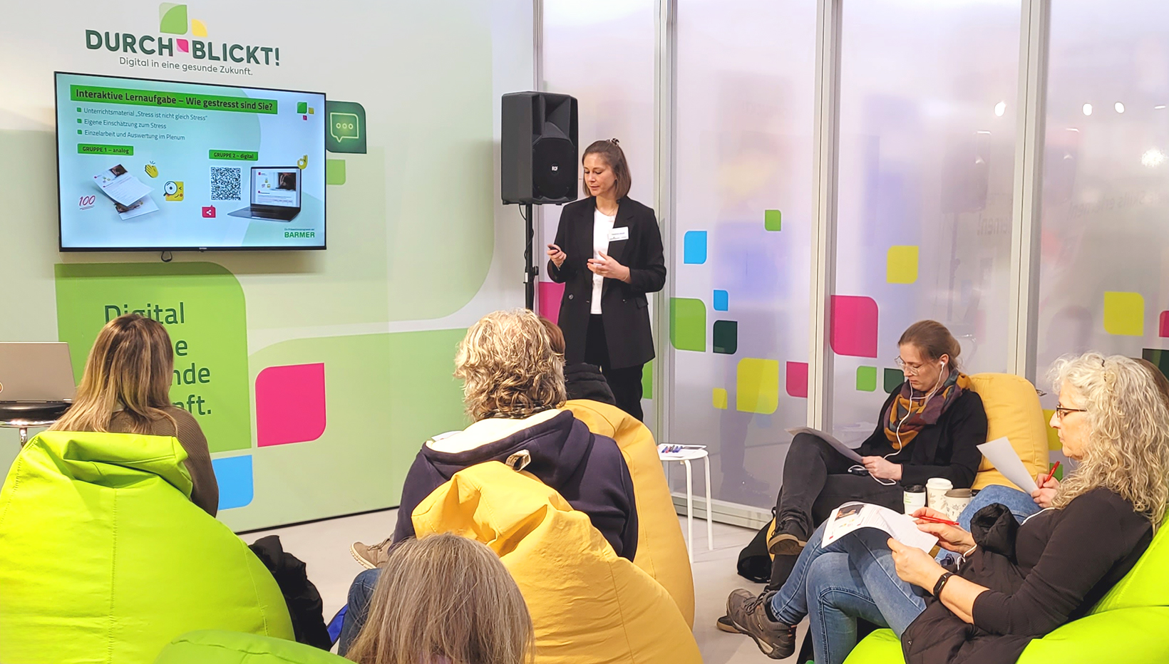 Frau hält einen Vortrag. Um sie herum sitzen Menschen.