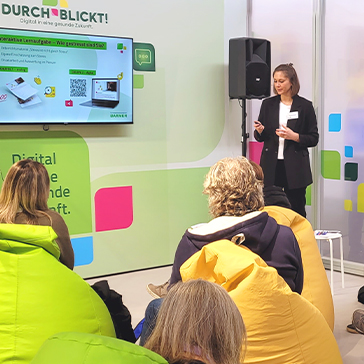 Frau hält einen Vortrag. Um sie herum sitzen Menschen.