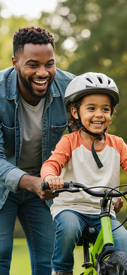 Vater hilft seinem Kind beim Fahrrad fahren. Beide lachen.