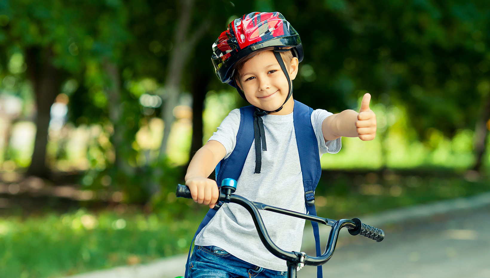 Kleiner Junge sitzt auf einem Fahrrad und hält lächelnd den Daumen frontal in die Kamera