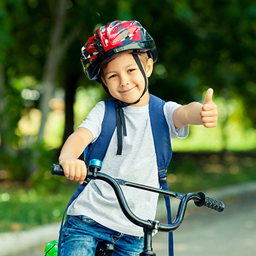Kleiner Junge sitzt auf einem Fahrrad und hält lächelnd den Daumen frontal in die Kamera