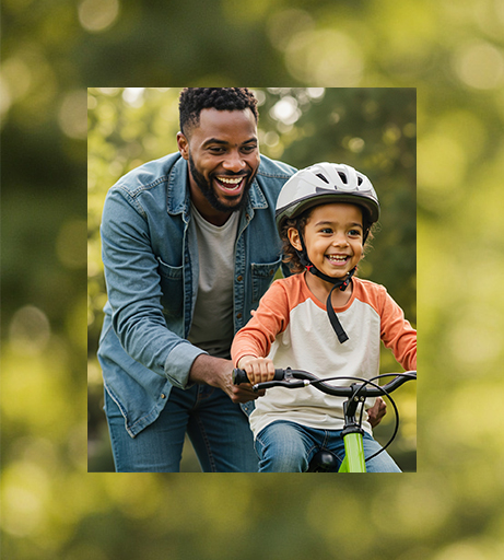 Vater hilft seinem Kind beim Fahrrad fahren. Beide lachen.