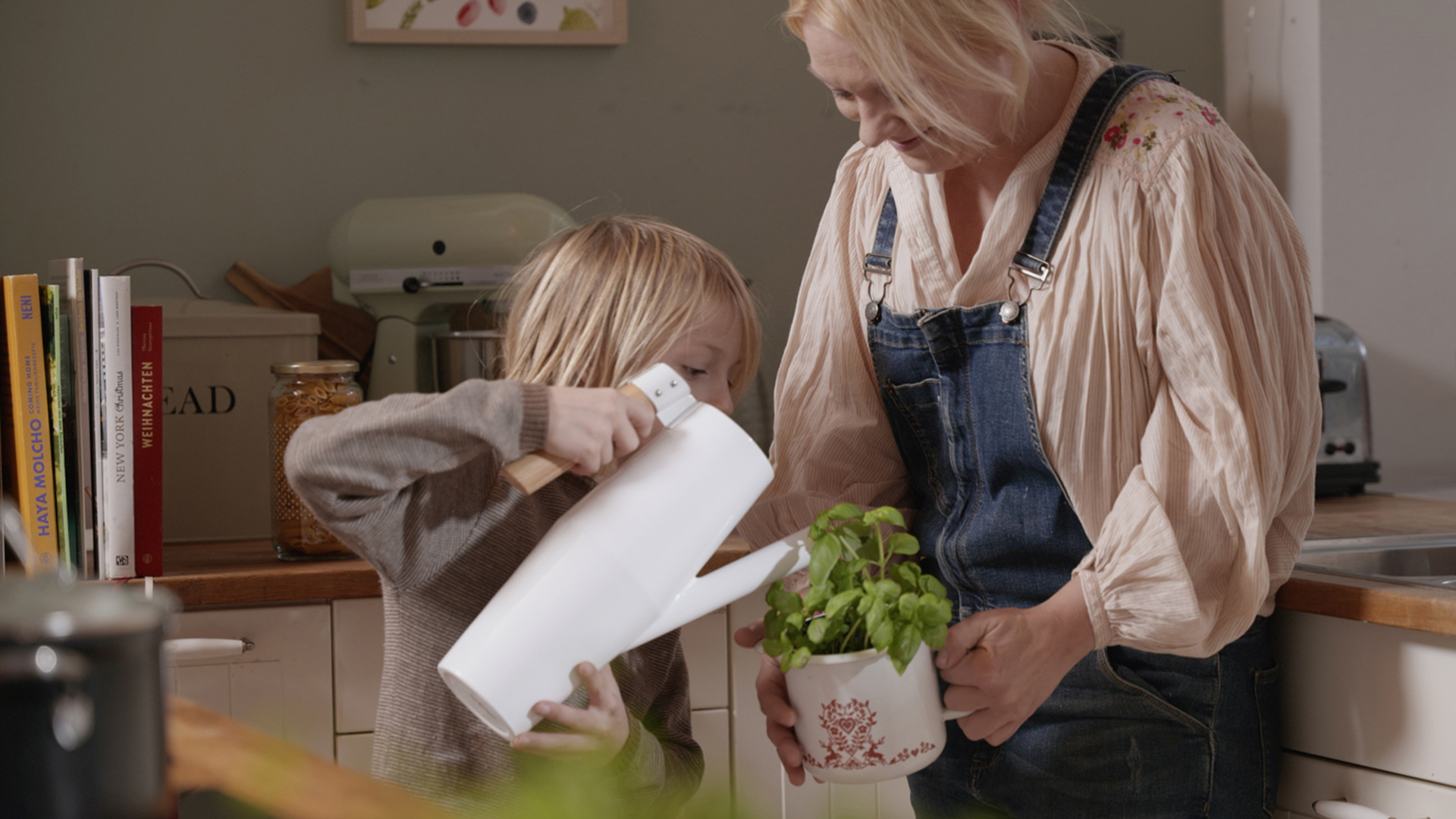 Kind gießt Basilikum, der von Mutter gehalten wird