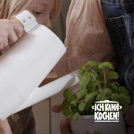 Kind gießt Basilikum, der von Mutter gehalten wird