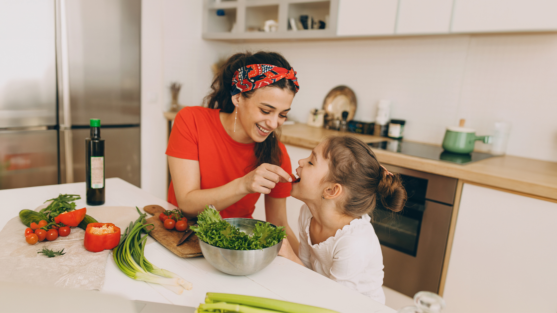 Mutter und Tochter naschen während des Kochens in der Küche eine Tomate