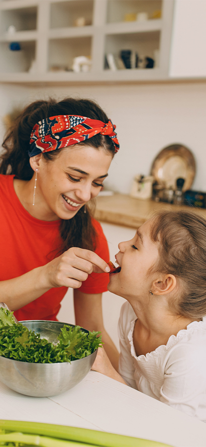 Mutter und Tochter naschen während des Kochens in der Küche eine Tomate