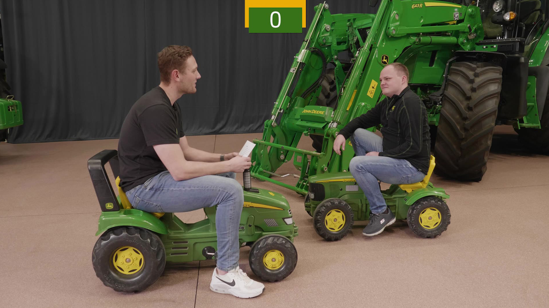 Zwei Männer auf grünen Kinder-Traktorspielfahrzeugen