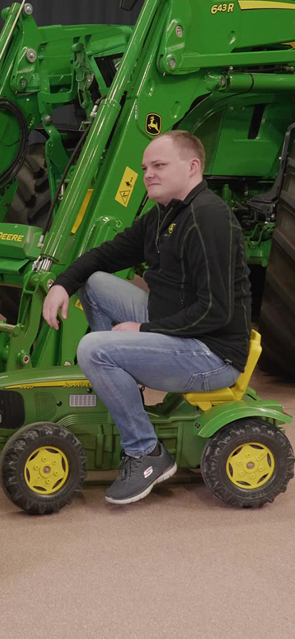 Zwei Männer auf grünen Kinder-Traktorspielfahrzeugen