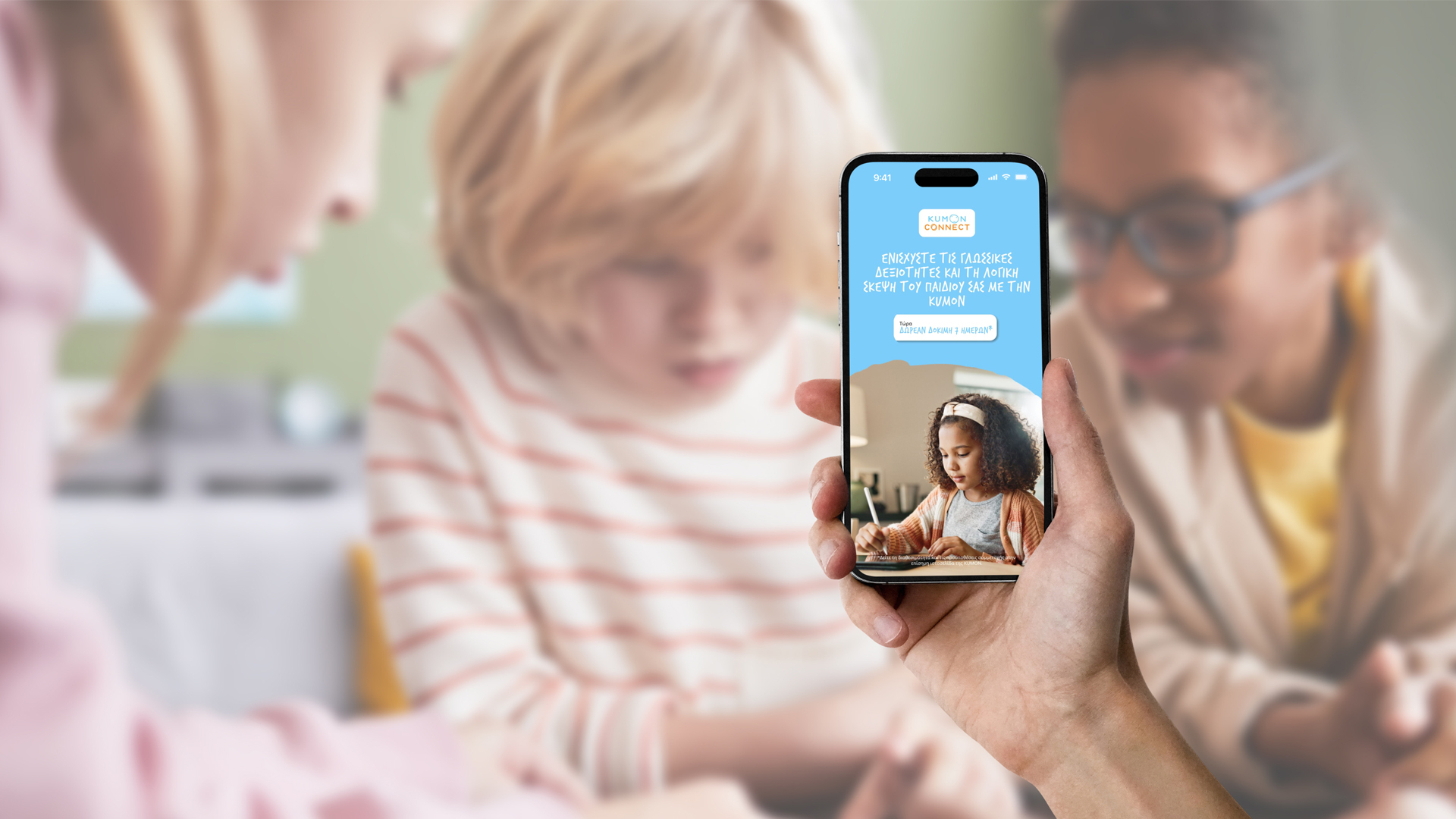 Hand mit Smartphone, das KUMON Connect App zeigt, vor Lernsituation mit Kindern und Lehrerin.