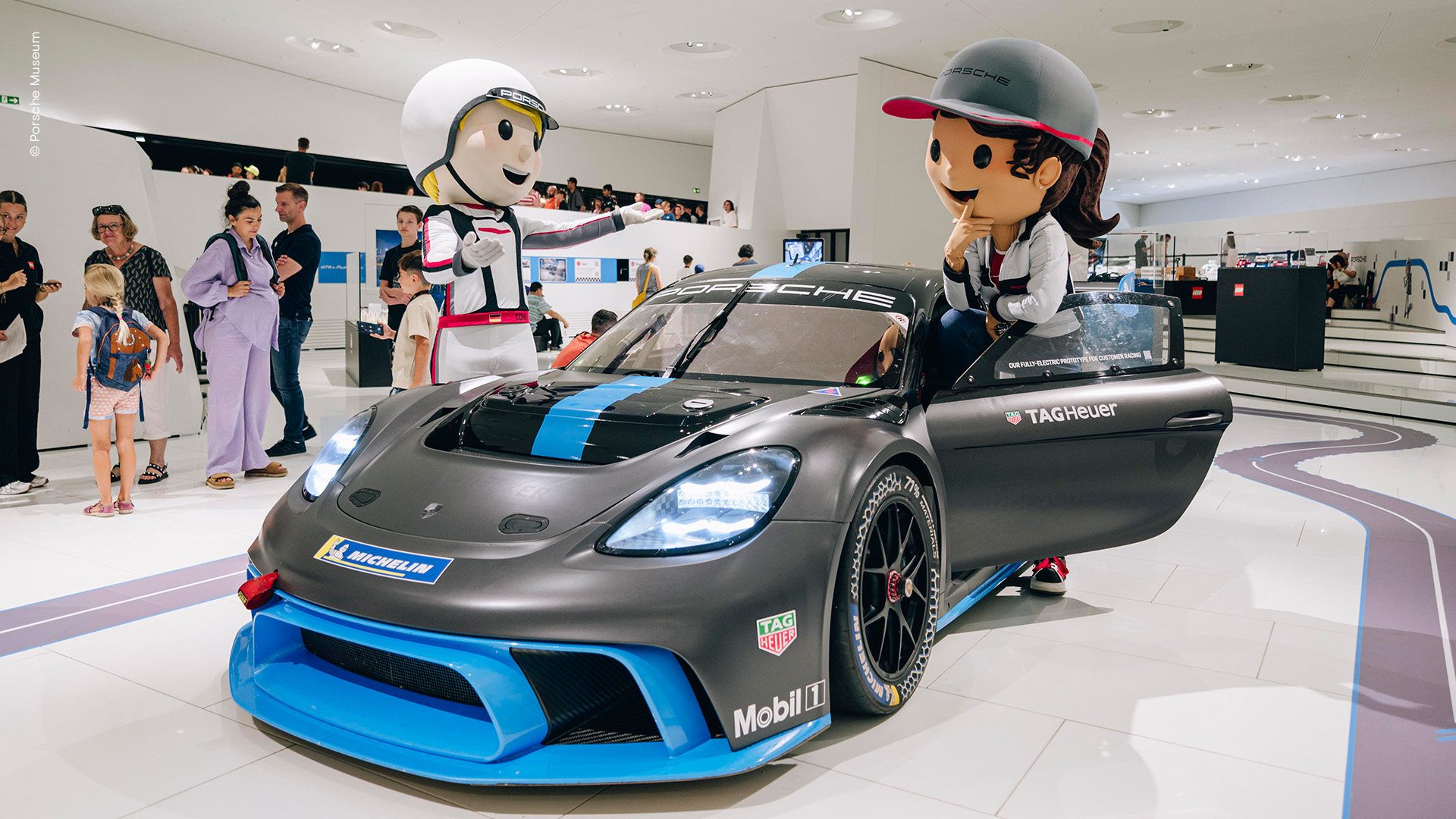 Zwei Rennfahrer-Maskottchen stehen an einem Porsche 