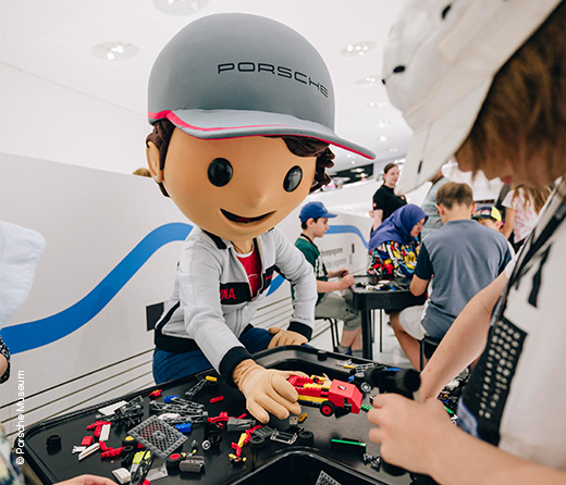 Rennfahrer Maskottchen reicht etwas einem Kind