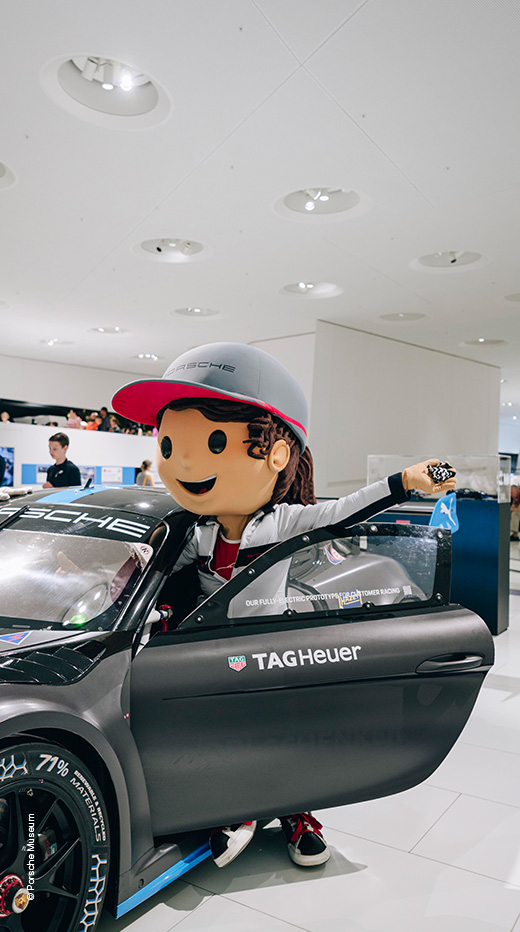 Rennfahrer Maskottchen steht in geöffneter Porsche-Tür