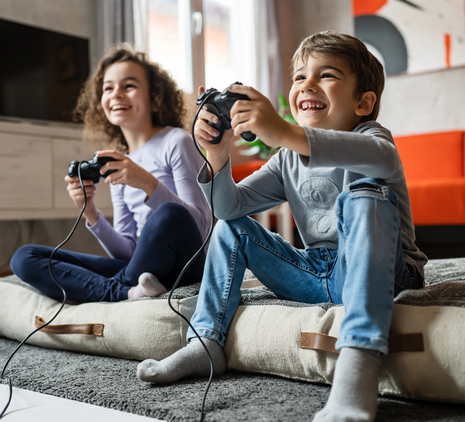 Ein Junge und ein Mädchen halten jeweils einen Spielecontroller in der Hand und lachen