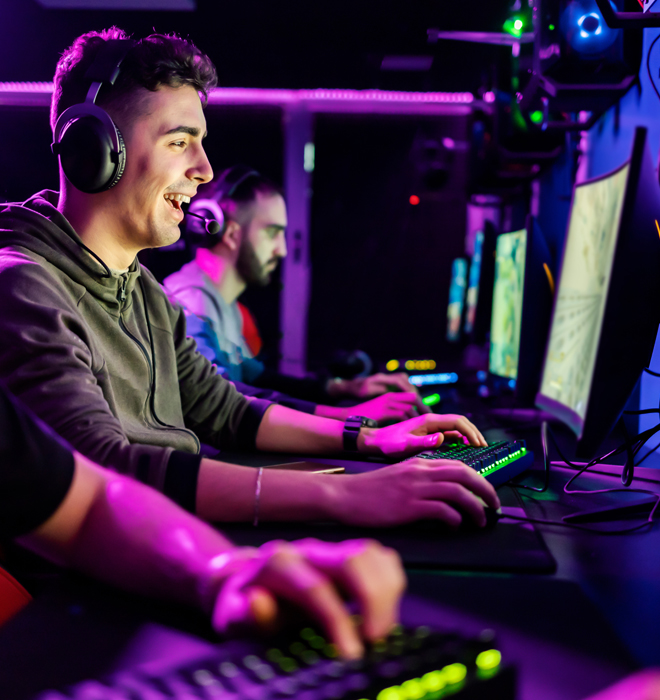 Junger Mann mit Kopfhörern sitzt vor einem Bildschirm und lacht.