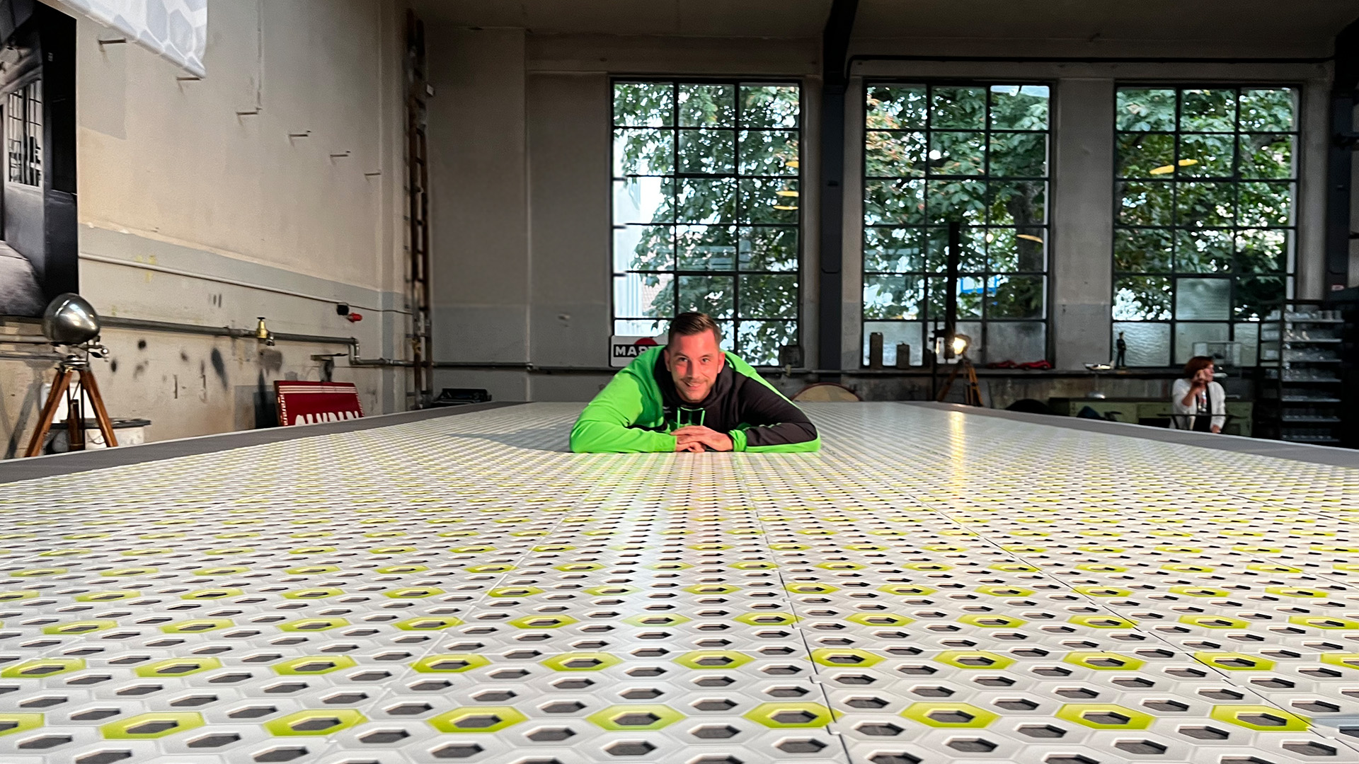 Mann in grüner Jacke liegt auf dem Boden und hat die Arme vorne zusammen. Er schaut frontal in die Kamera.