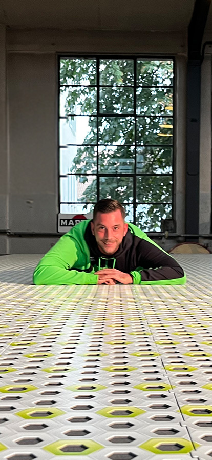 Mann in grüner Jacke liegt auf dem Boden und hat die Arme vorne zusammen. Er schaut frontal in die Kamera.