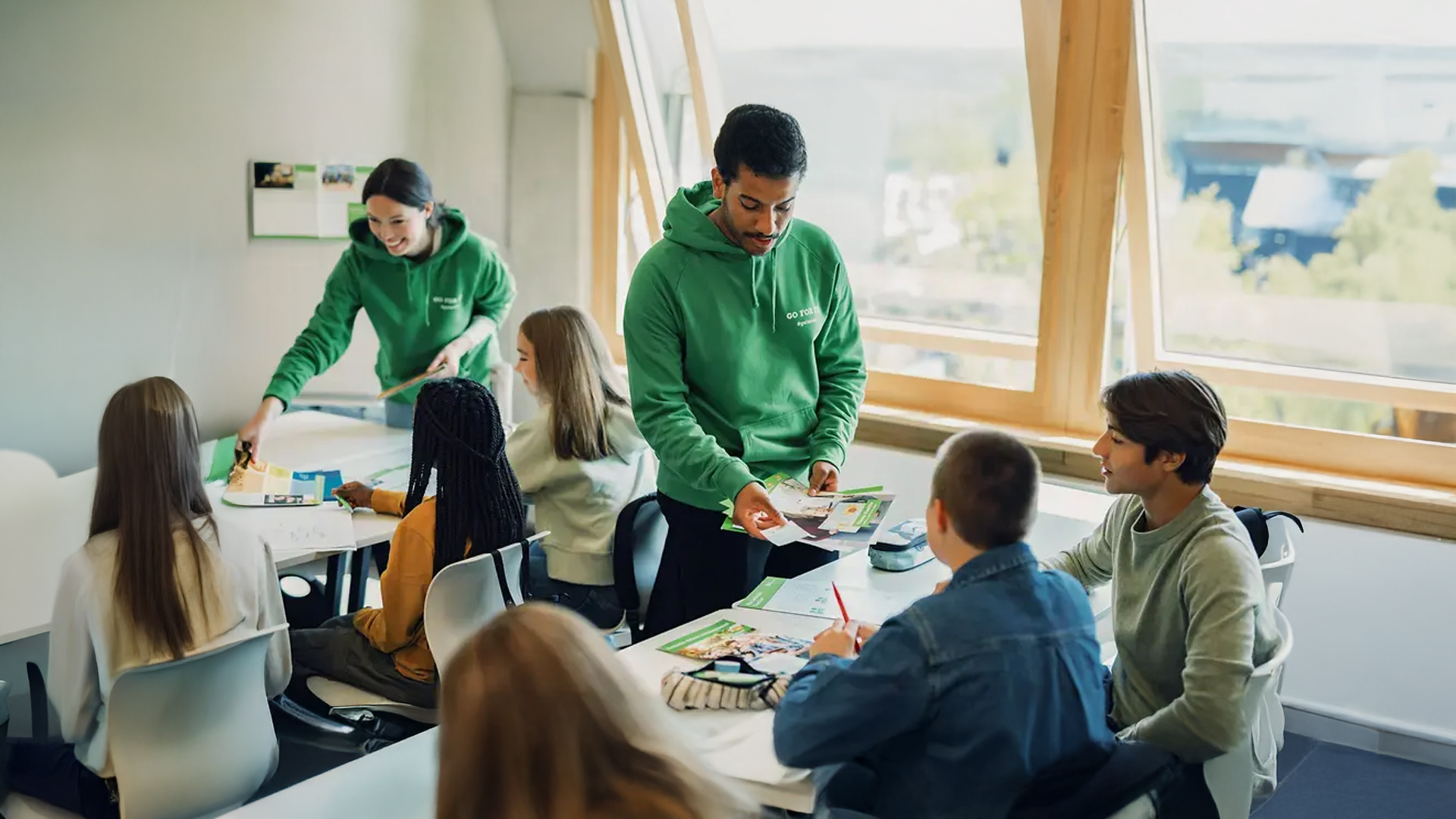 Lehrer erklärt zwei Schülern etwas im Klassenzimmer.