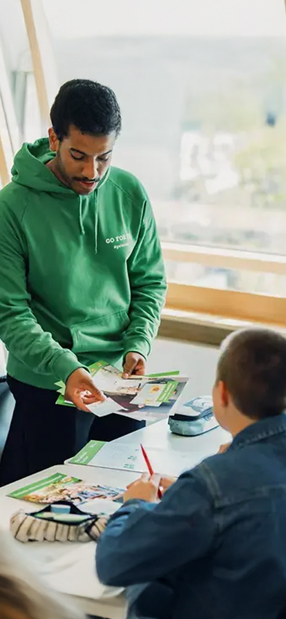 Lehrer erklärt zwei Schülern etwas im Klassenzimmer.