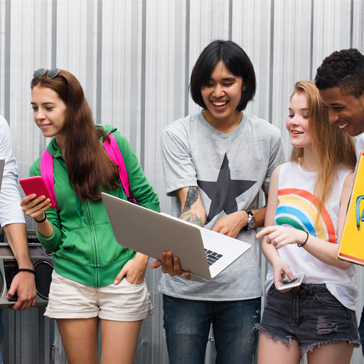 Gruppe Jugendliche sitzen mit Laptop zusammen und lachen.