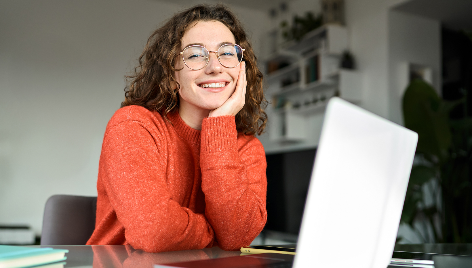 Junge Frau sitzt lächelnd vor Laptop.