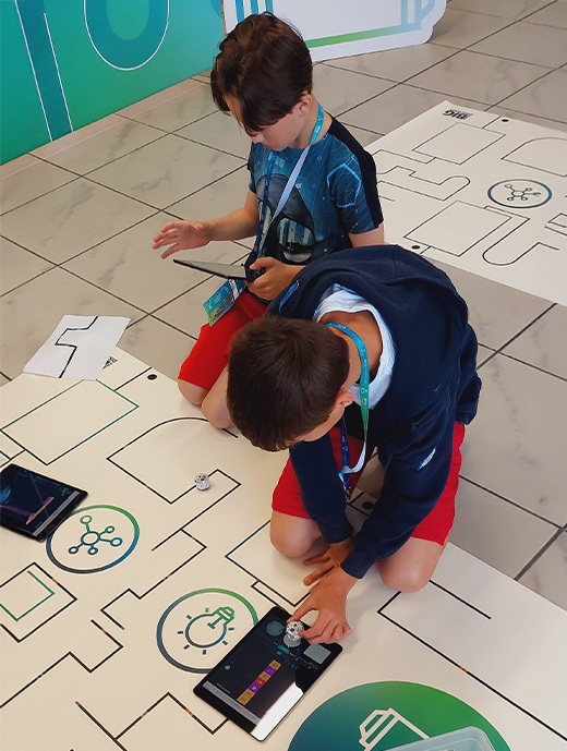 Zwei Kinder sitzen auf dem Boden und schauen auf eine Zeichnung, die darauf liegt.