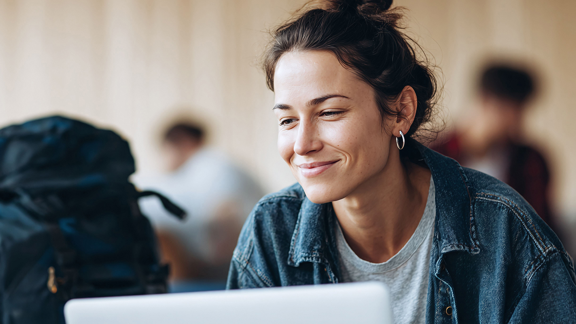 Junge Frau mit braunen Haaren schaut lächelnd auf ein Laptopdisplay